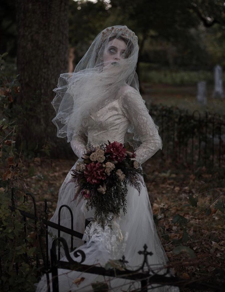 a woman dressed in white and wearing a veil with flowers on her head, standing next to a wrought iron fence