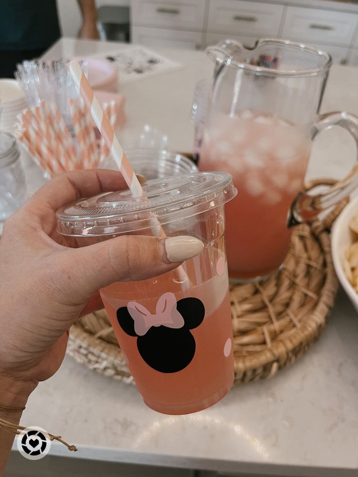 a person holding a cup with straws in it and minnie mouse on the lid