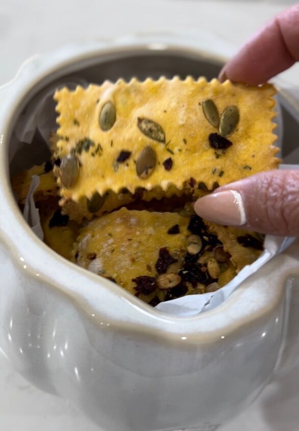 a hand holding a cracker over a bowl filled with some kind of food on top of it