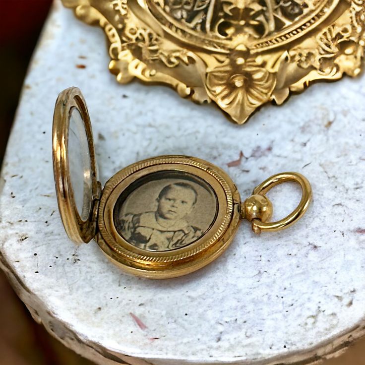 Step back in time with this exquisite late Victorian or early Edwardian gold-filled mourning locket pendant. 🕰️🌹 This treasured piece encases a sepia picture of a little boy behind a glass window, preserving a poignant memory from the past. Open it to reveal the picture protected by another round glass frame. 📸✨  The picture is not straight but is placed sideways in the locket so the person wearing it on a chain can easily take it in her hand and look at the little boy.  Though unsigned, this Antique Medallion Jewelry For Commemoration, Antique Commemoration Medallion Jewelry, Victorian Jewelry With Coin Pendant, Victorian Yellow Gold Medallion Locket Necklace, Vintage Yellow Gold Locket Necklace For Memorial, Vintage Yellow Gold Memorial Locket Necklace, Antique Yellow Gold Locket Necklace For Keepsake, Victorian Medallion Jewelry With Historical Design, Victorian Round Pendant Jewelry For Commemoration