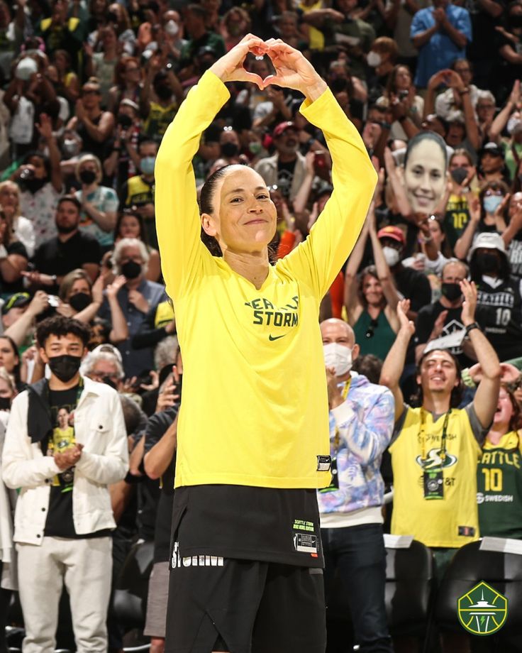 a man in yellow shirt and black shorts holding his hands up to the air while people watch