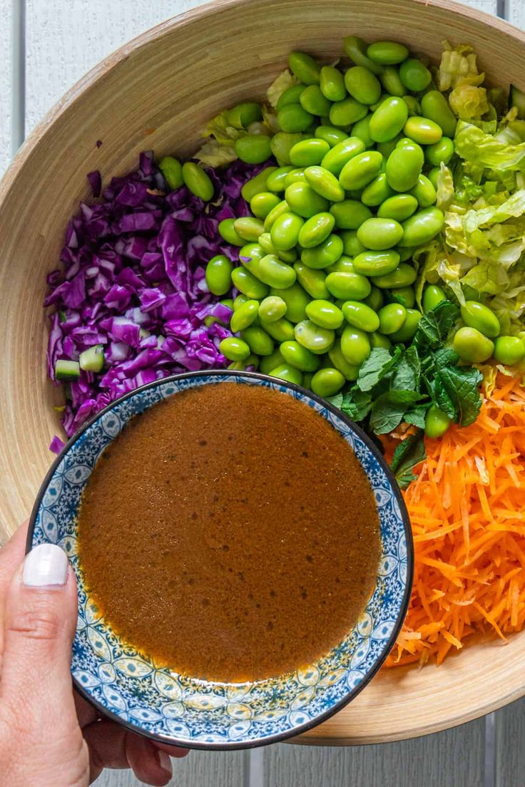 a person holding a bowl filled with different types of vegetables and dipping sauce in it