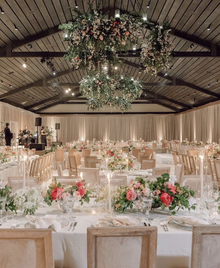 a banquet hall with tables and chairs covered in white linens, floral centerpieces and hanging chandeliers