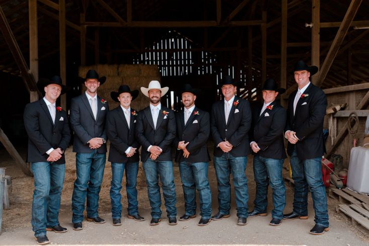 a group of men standing next to each other in front of a wooden structure wearing cowboy hats