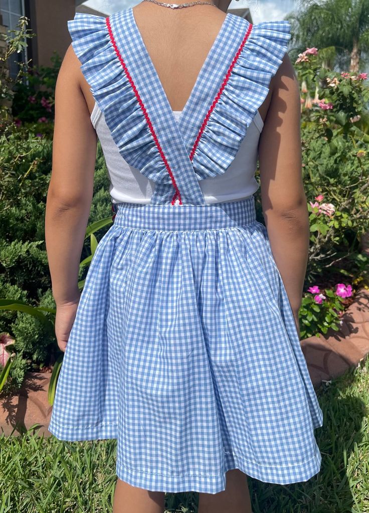 This is a blue and white gingham Pinafore dress with red detailing. It has a clasp closure at the waist with a button facade exterior. The top is double layered and the skirt contains a white cotton layer underneath.  The material is a soft cotton mix. Dresses are made to order according to the chart. If you would like a specific measure or adjustment please include this when placing your order. For larger sizes (little girl/big girl) there will be a price increase. Spring Sleeveless School Uniform Dresses, Blue Cotton Dress With Ruffled Skirt, Gingham Dresses For School In Spring, Preppy Cotton Dress For Picnic, Plaid Summer Dress For School, Plaid Dresses For Summer School, Plaid Dresses For School In Summer, Pinafore Dress, Gingham