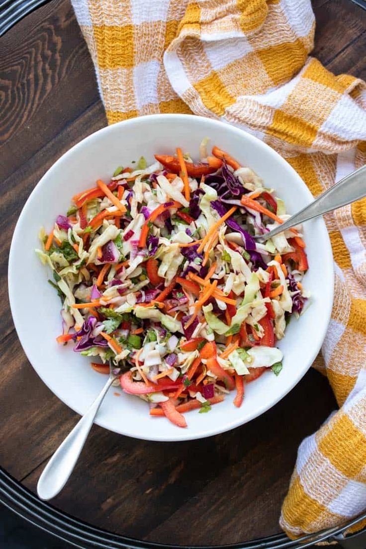 a bowl filled with coleslaw and carrots on top of a wooden table