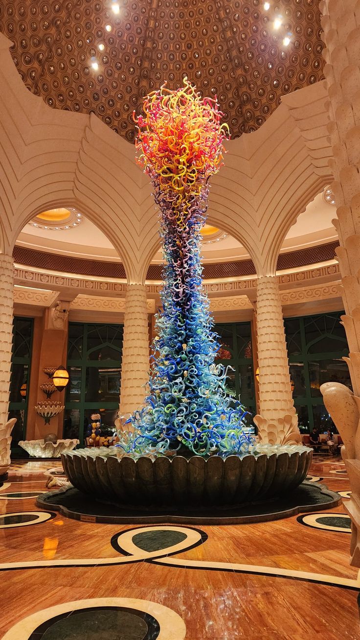 a very tall glass sculpture in the middle of a room with chandelier above it