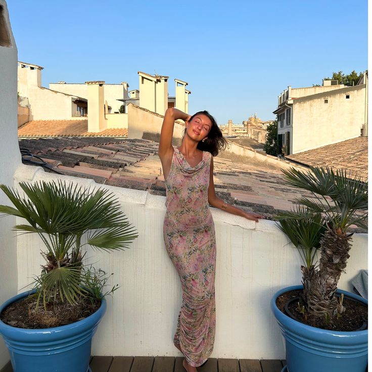 a woman standing on a balcony next to two potted plants