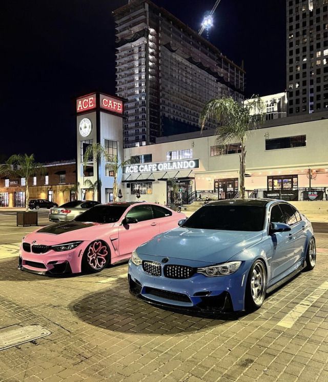 two cars parked in front of a building at night with palm trees on the sidewalk