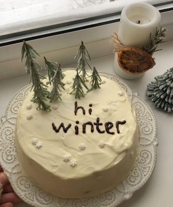 a cake with the words hi winter written on it next to some pine trees and candles