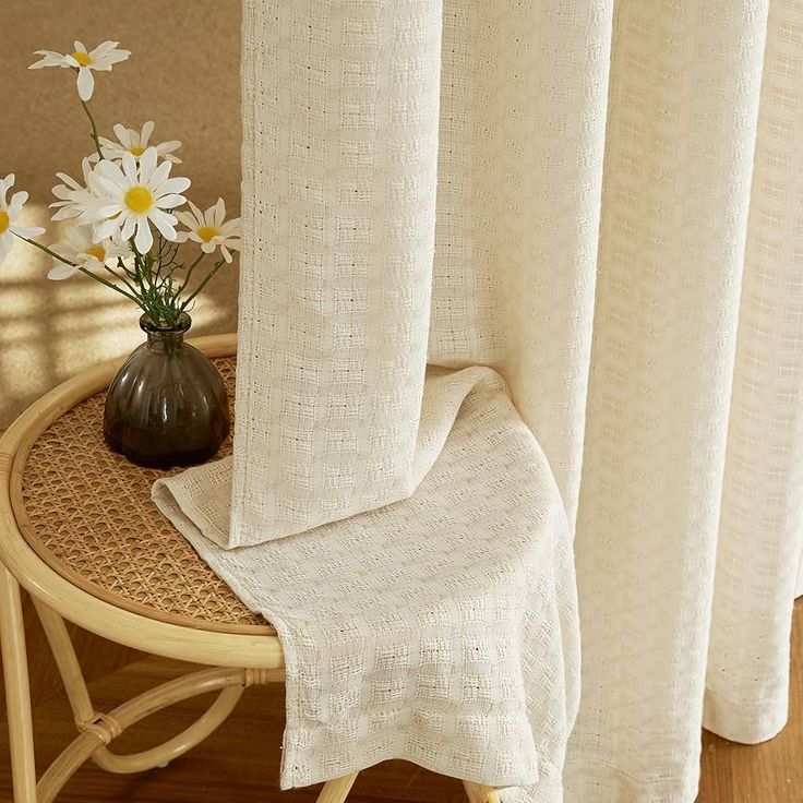 a vase with flowers sitting on top of a table next to a window covered in white curtains