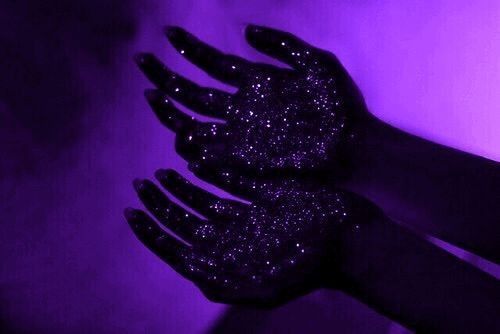 a hand with black glitter on it is holding something in the air and purple light