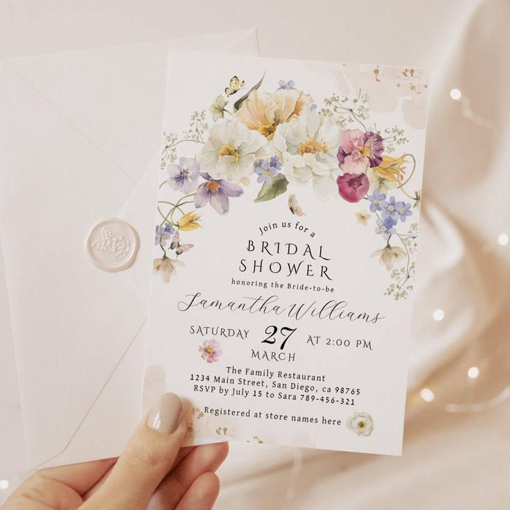 a person holding up a wedding shower card with flowers on the front and bottom, in front of a white background