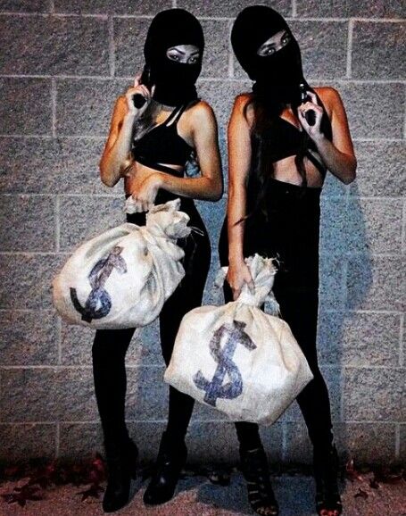 two women wearing masks and holding bags in front of a brick wall