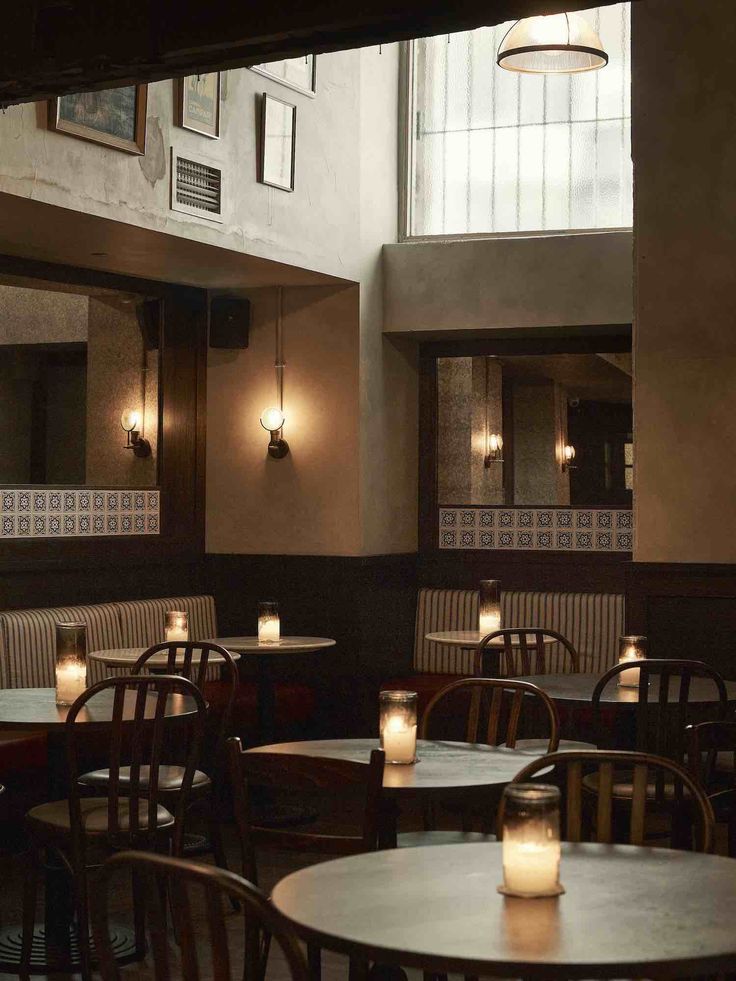 the interior of a restaurant with tables and chairs, lit by candle lights on each table