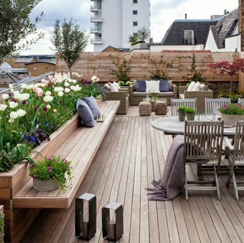 an outdoor patio with wooden benches and tables surrounded by flowers on the side of it