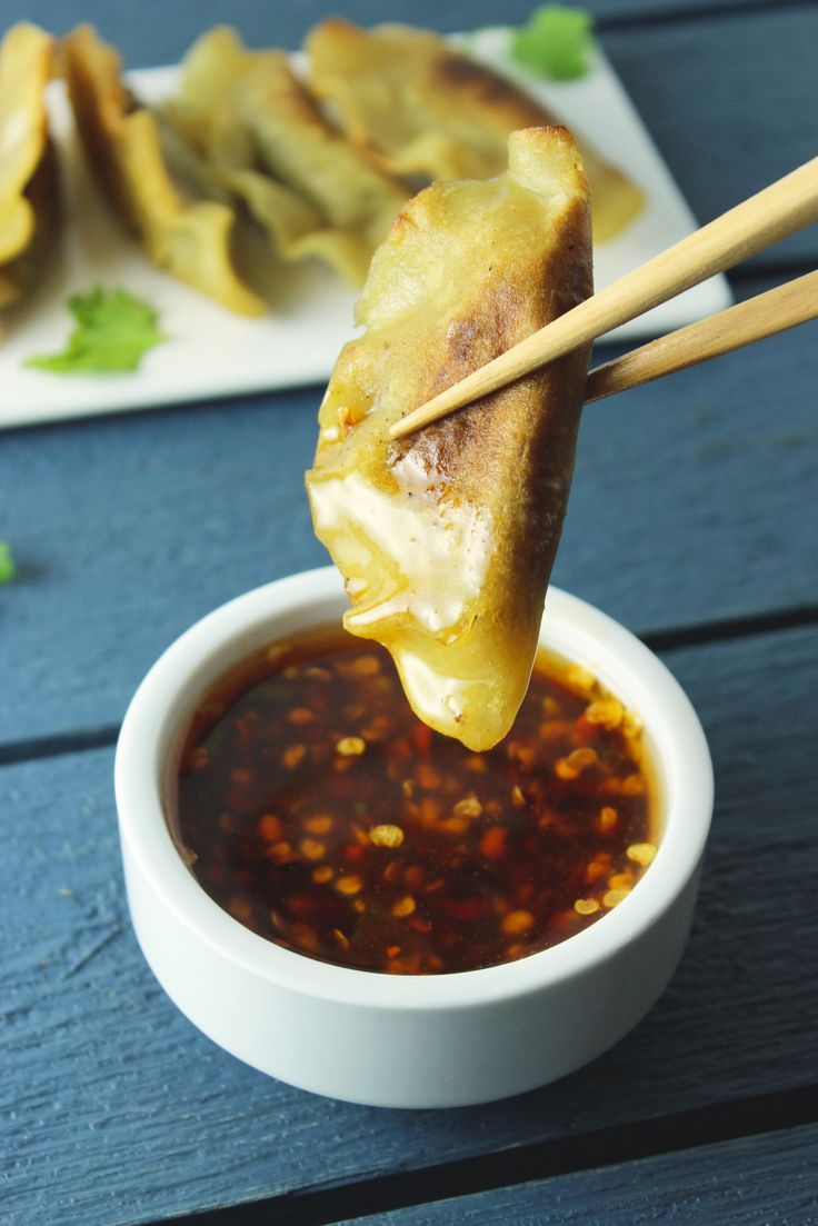 some food is being held up by chopsticks in a bowl with sauce on the side