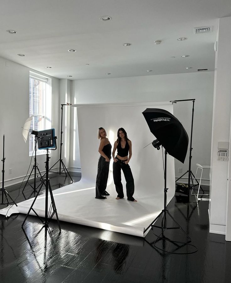 two women are standing in front of a white backdrop with black lights and umbrellas