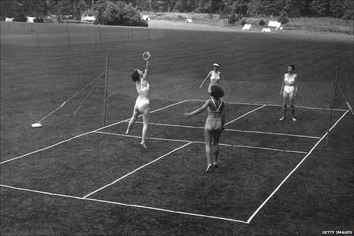 four people are playing tennis on the grass in an old black and white photo, with one person reaching up to hit the ball