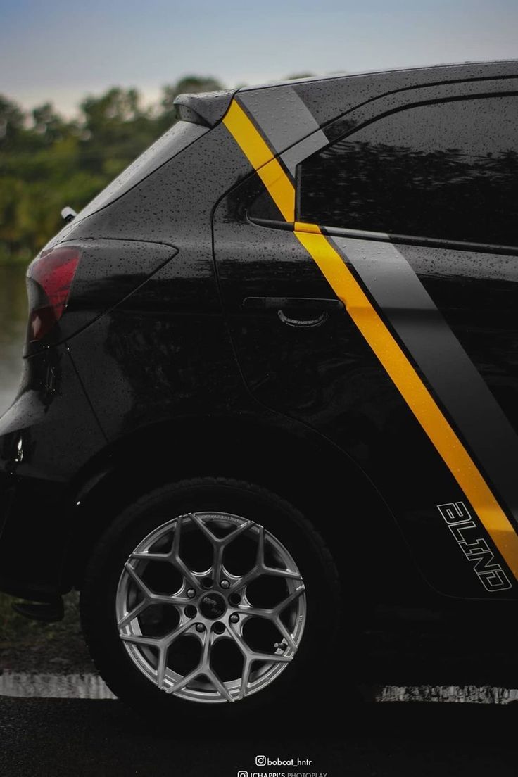 a black car with yellow stripes parked on the side of the road next to water