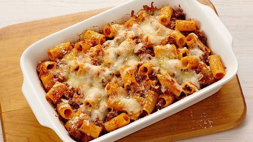 a casserole dish filled with pasta and meat in a white baking dish on top of a wooden table