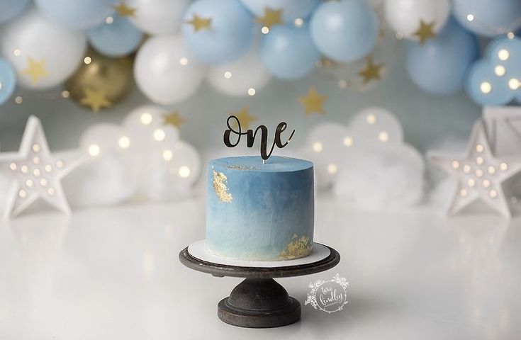 a blue and white cake sitting on top of a table next to some balloons in the background