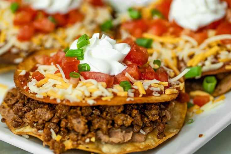 some taco shells are topped with cheese and sour cream on the top, along with green onions