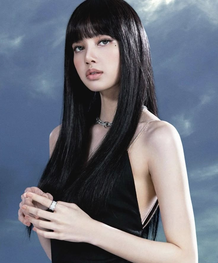 a woman with long black hair standing in front of a blue sky and cloudy background