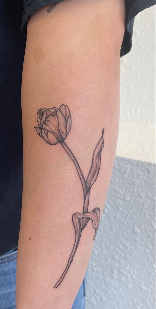 a black and white photo of a flower tattoo on the right arm, with an outline of a single tulip