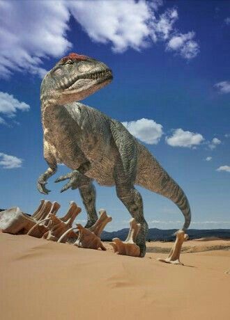 a large dinosaur standing on top of a pile of logs in the sand with blue sky and clouds behind it