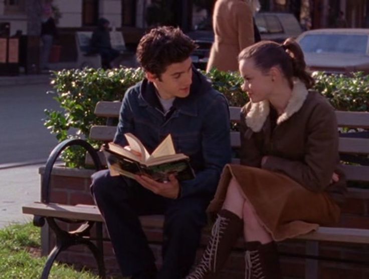 a man and woman sitting on a bench reading books in front of each other while looking at an open book