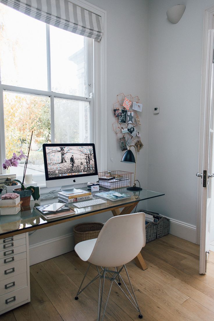 a desk with a computer on top of it in front of a window next to a chair