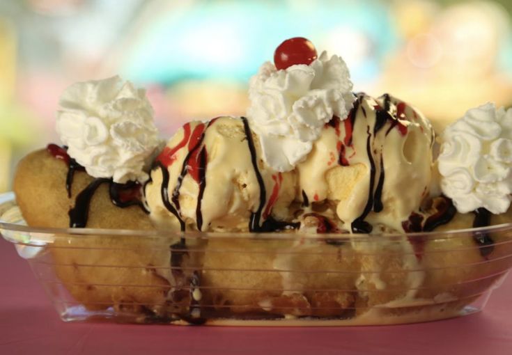 an ice cream sundae with cherries and whipped cream in a glass dish on a pink table