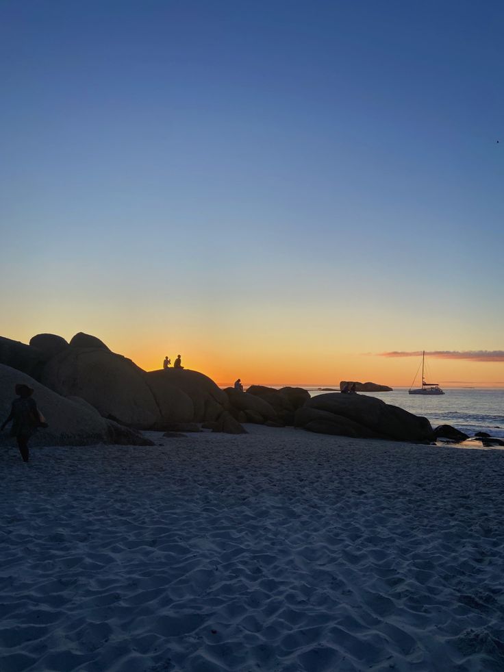 two people are standing on the beach watching the sun rise over the water and rocks