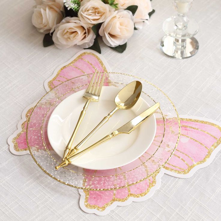 a table setting with pink and gold placemats, silverware and white flowers