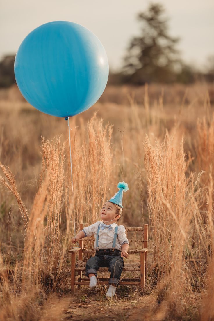 a little boy sitting in a chair with a blue balloon