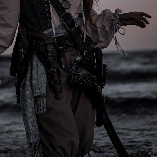 a man dressed in pirate garb walking on the beach with his hands out to the side