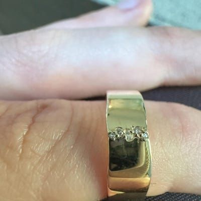 a person's hand with a gold ring on top of their finger and diamond set in the middle