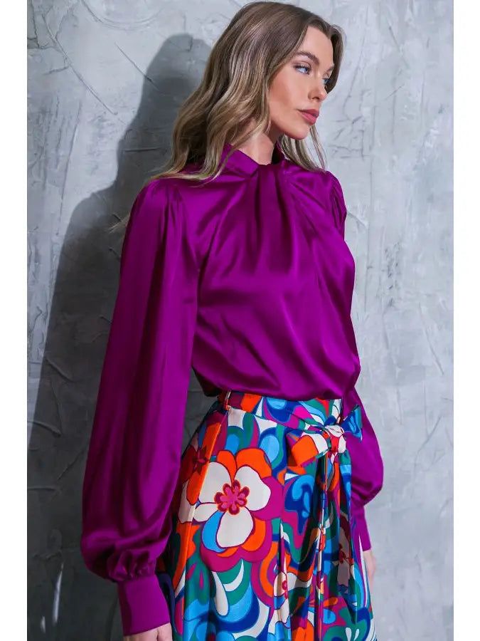 This solid blouse top features vibrant satin fabric, high neckline with twisted detail, a long sleeve with cuff, and back button closure. Fabric: Self : 95% Polyester 5% Spandex Color: Dark Orchid