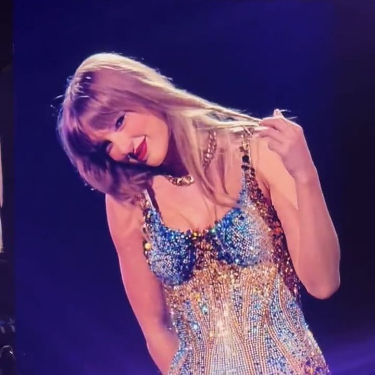 taylor swift performing on stage in a sequined dress with her hands behind her head