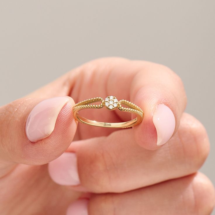 a woman's hand holding a gold ring with a diamond on it and the middle finger