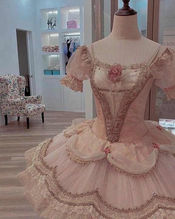 a dress on display in a room with wooden flooring and white walls, decorated with pink flowers