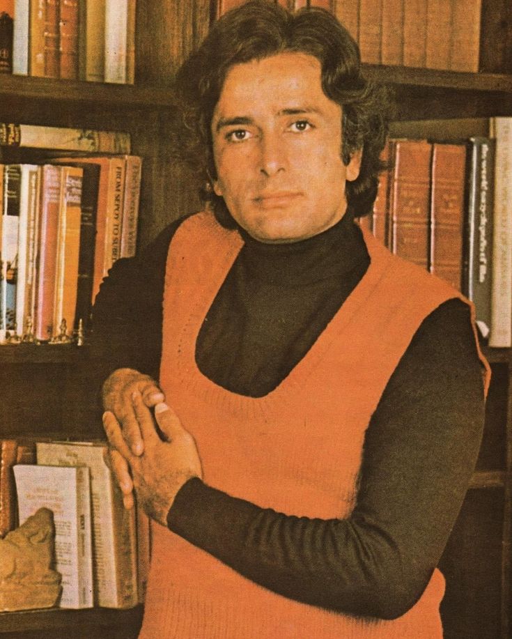 a man standing in front of a bookshelf with his arms crossed and looking at the camera