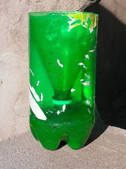 a green glass vase sitting on top of a cement wall next to a stone wall