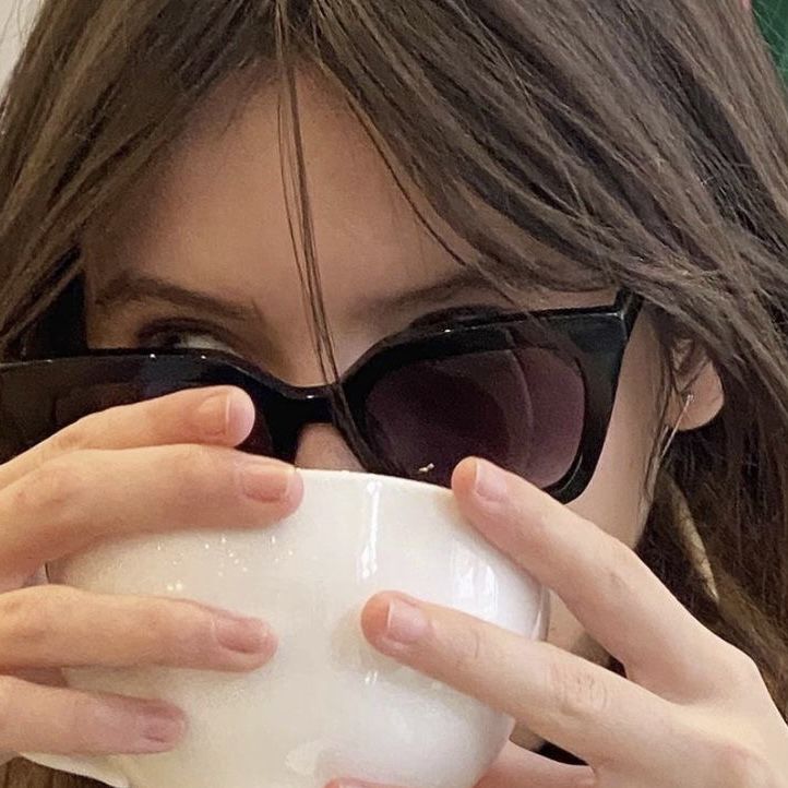 a woman wearing sunglasses drinking from a white cup with her hands on the top of it