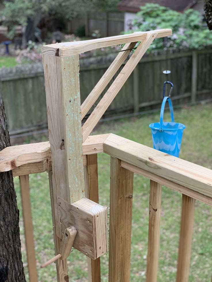 a blue bucket sitting on top of a wooden rail next to a tree trunk in a yard