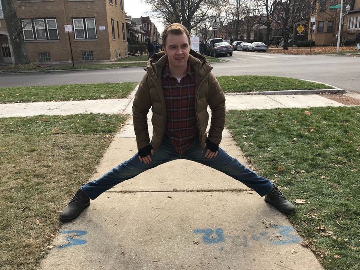 a young man sitting on the edge of a sidewalk in front of some buildings and grass