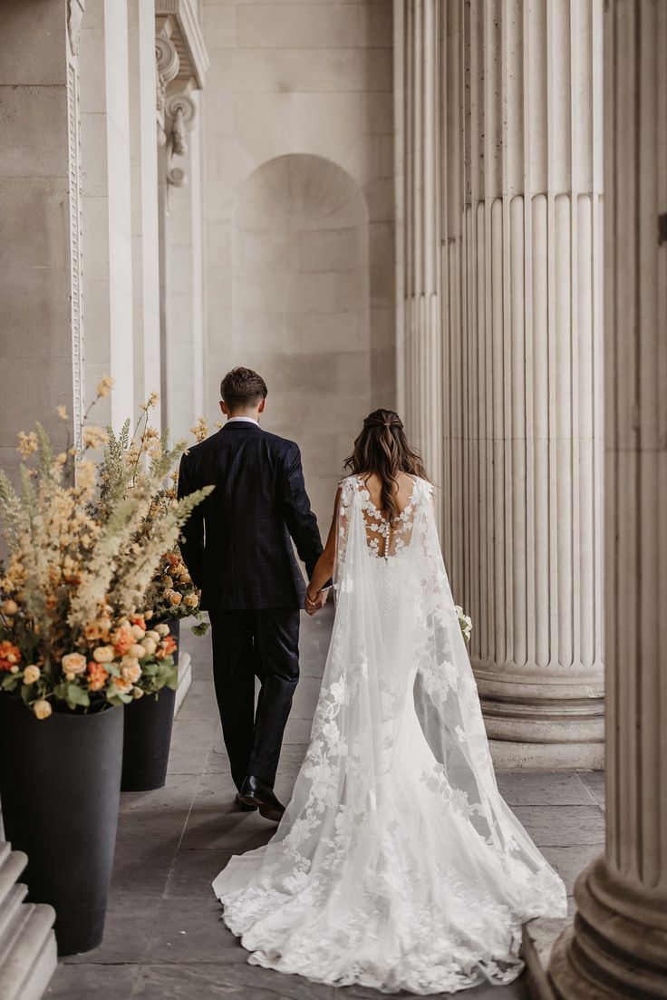 a bride and groom holding hands walking down the aisle in an old building with columns