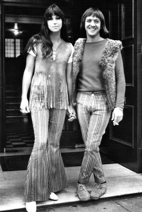 two young women standing next to each other in front of a store door wearing striped pants and vests