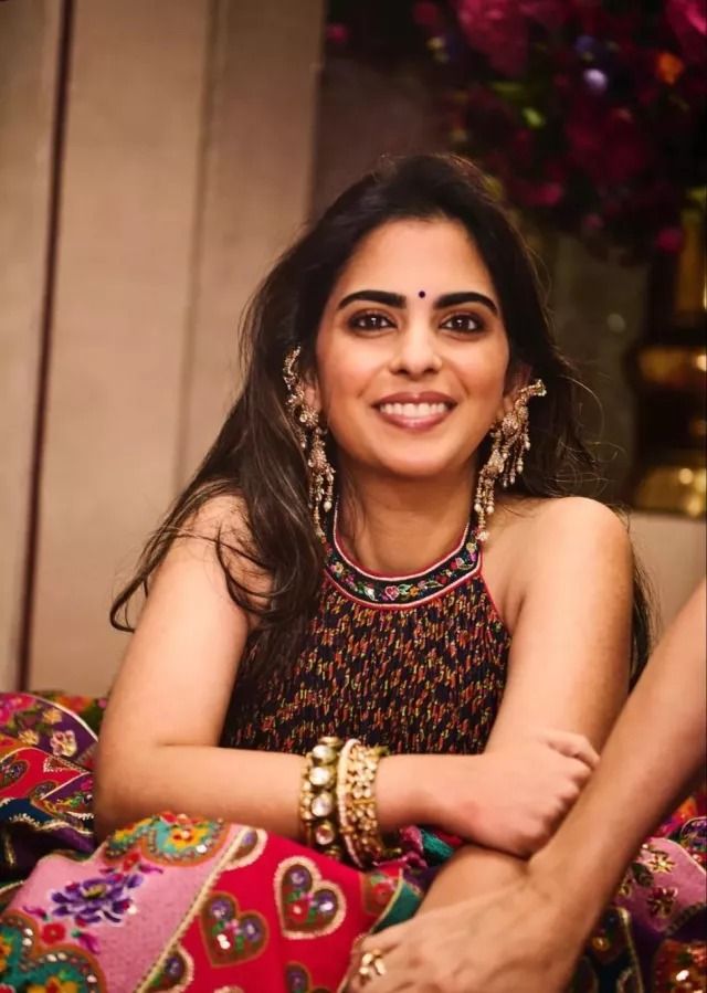 a woman sitting on top of a colorful couch next to a flower covered wall and smiling at the camera